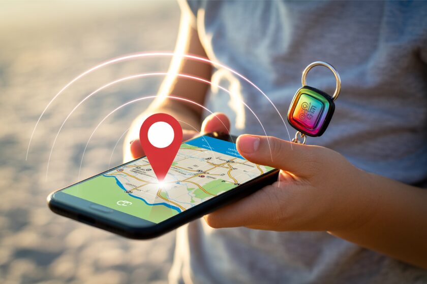 Реалистичное фото цветного брелока с GPS-маячком, прикреплённого к смартфону ребёнка, который держит его в руке, с тонкими линиями GPS-сигнала, соединяющимися со спутниками.